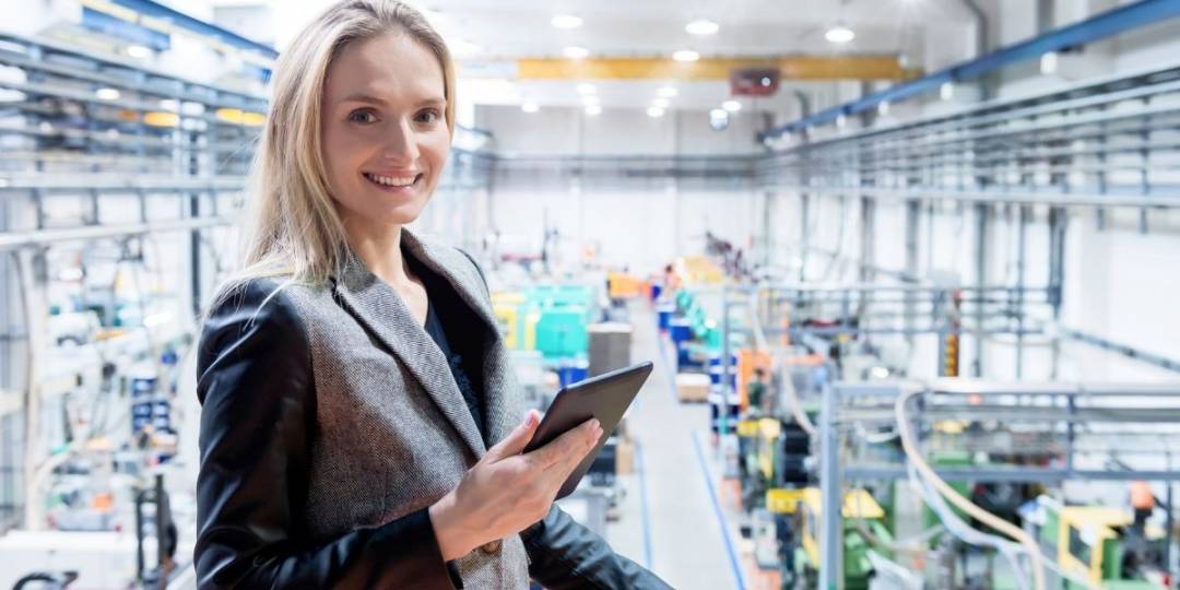 A smiling manager with a tablet computer in her hands, used to keep track of production. She works in a manufacturing plant.